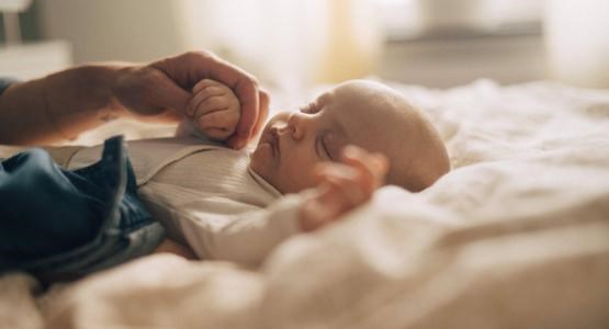 En bebis sussar söt på rygg i mammas och pappas säng.