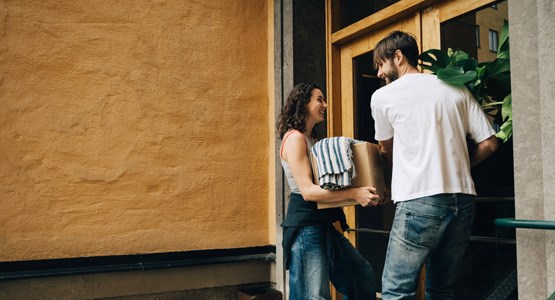 Par som bär in flyttlådor genom en lägenhetsport.