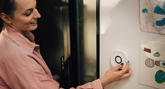 En kvinna står vid en ytterdörr och knappar på en knappsats till ett hemlarm.