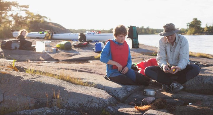 En far och en son sitter vid klipporna vid havet och äter.