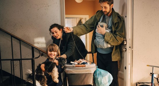 Familj med små barn på väg ut i trapphus med barnvagn och hund.