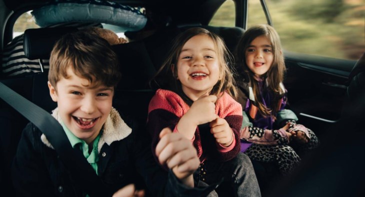 Tre barn sitter i baksätet på en bil och skrattar högt.