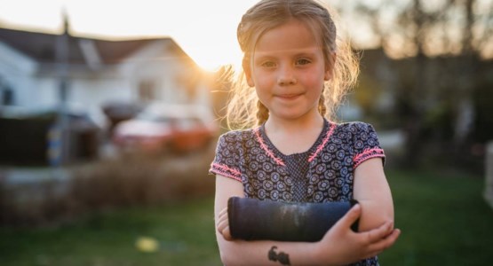 En liten flicka med gipsad arm ler mot kameran.