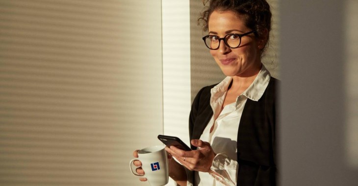 Kvinna läser på mobilskärm med kaffekopp i handen.