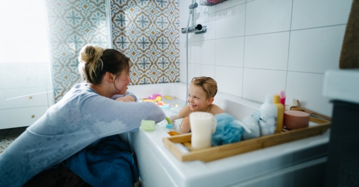 Barn i badkar leker med sin mamma.