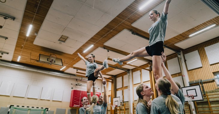 Åtta tjejer i en gymnastikhall som tränar cheerleading.