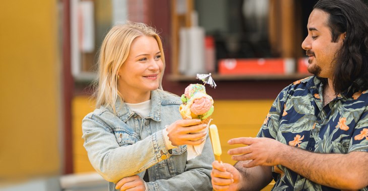 En kvinna och en man sitter på en bänk och äter glass.