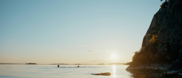 Två personer som badar i solnedgång ses på långt avstånd.
