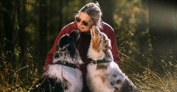 Eva Olausson sitter på huk och gosar med sina två hundar i skogen.