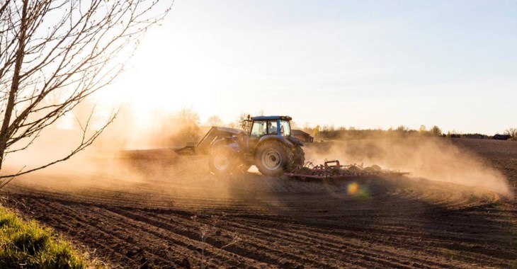 En lantbrukare harvar på sin åker i en grön traktor.