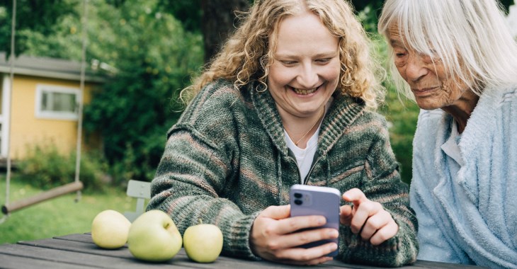 En ung och en gammal kvinna läser i mobiltelefonen