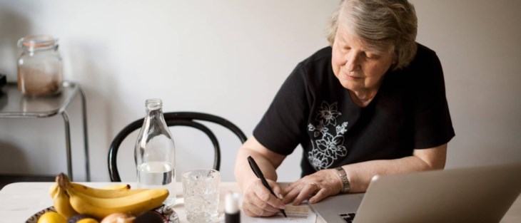 Foto på äldre kvinna sitter vid datorn och kollar sin sparränta på sitt fasträntekonto.