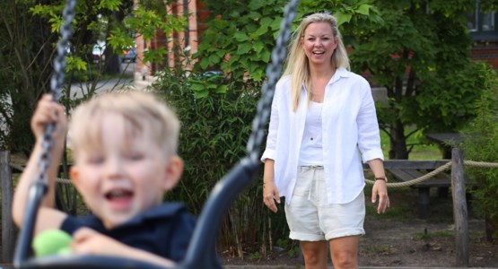 Kvinna gungar sin son på lekplats.