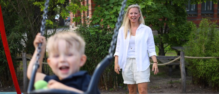 Kvinna puttar på barn i gunga på lekplats.