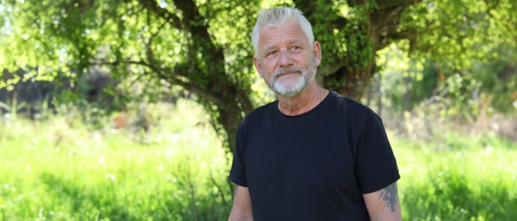 Man i i övre medelåldern står i somrig trädgård. 