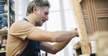 En manlig möbeltapetserare kl'r om en fåtölj.