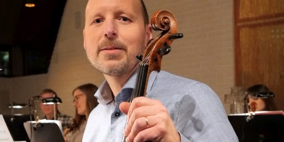 Man i orkester som håller i en fiol och tittar in i kameran
