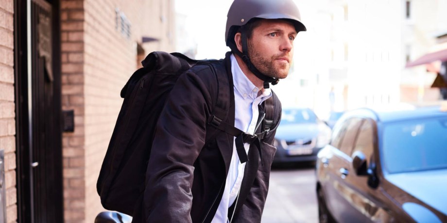 Man med ryggsäck och cykelhjälm blickar ut över trafikerad gata.