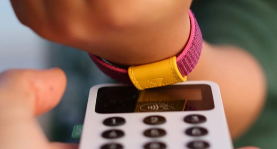Ett barn betalar genom att blippa sitt armband mot kortläsare.