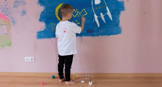 Ett litet barn målar en rymdraket med starka färger på en vit vägg.