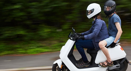 Två ungdomar på vit moped.