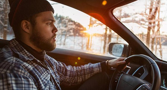 Man kör bil i vinterlandskap.