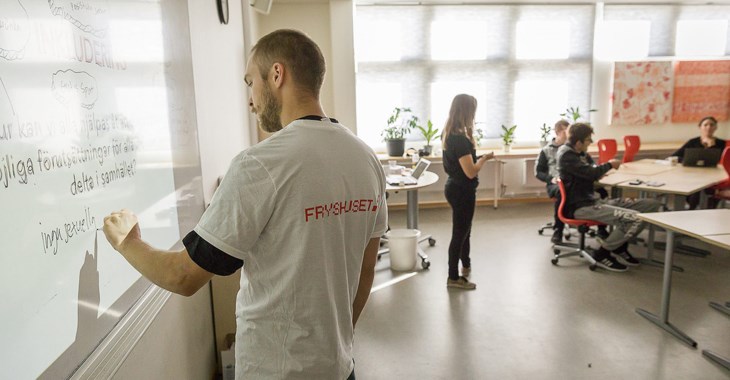 En kille skriver på en whiteboard i ett klassrum.