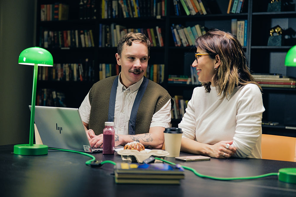 Två personer jobbar tillsammans vid laptop, i cafémiljö.