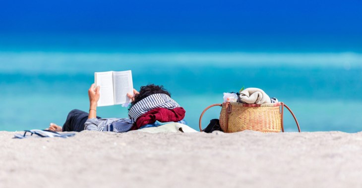 En kvinna ligger på stranden och läser en bok.