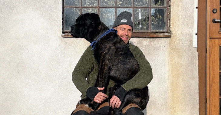 Gustav Ovland sitter utanför sitt hus med en av sina hundar i knät.