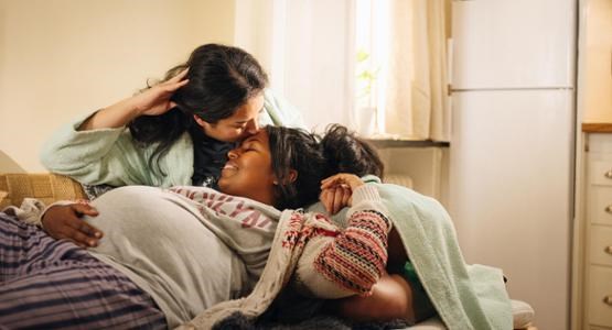 Gravid kvinna ligger i partners knä i soffan.