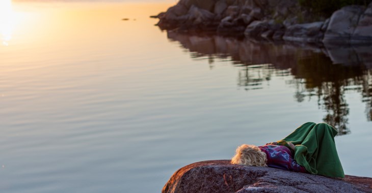 Foto på person som ligger på ett berg och blickar ut över solnedgången.