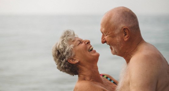 Äldre par kramas på stranden, klädda för bad.