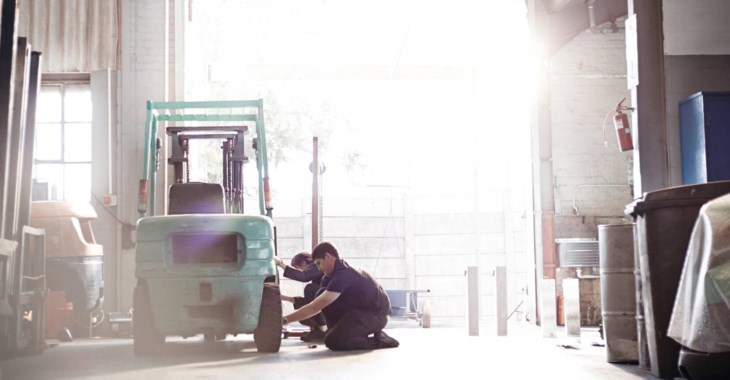 Två mekaniker byter däck på gaffeltruck.