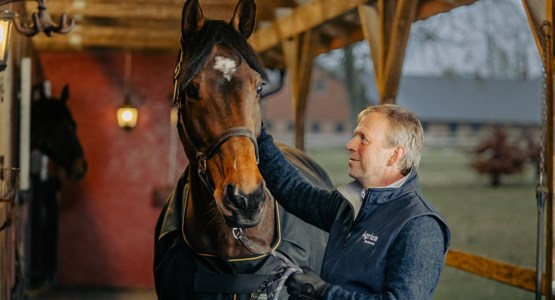 Ryttaren Jens Fredricsson klappar en brund häst på manen.