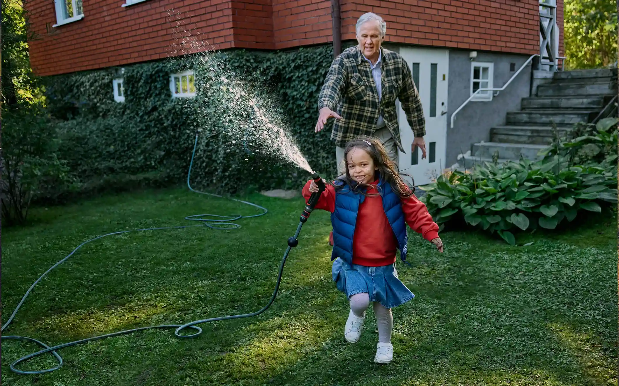 Äldre man jagar sitt barnbarn som håller i en vattenslang