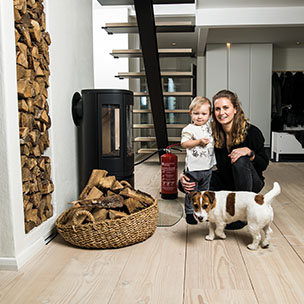 Mamma, dotter, hund framför eldstad. Bild.