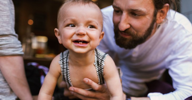 En pappa håller i sitt lilla barn som skrattar.