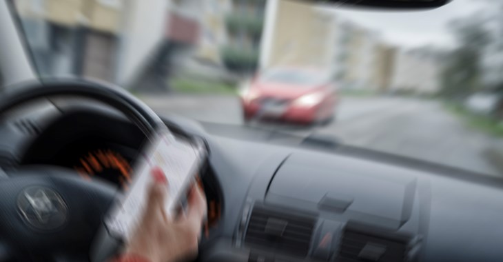 Kvinna kör bil och håller mobil i handen.