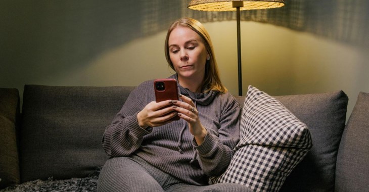 En kvinna sitter i en soffa och kollar på sin mobil.