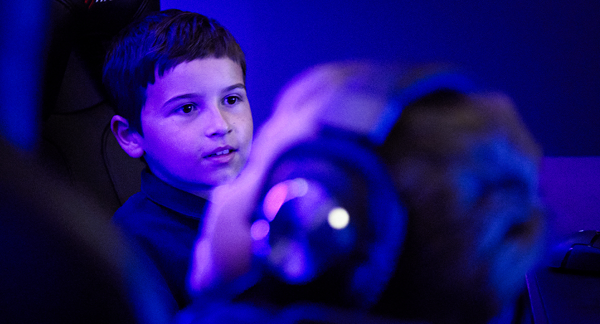 En pojke spelar datorspel i ett rum upplyst i blått och lila.