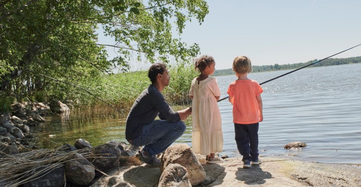 Två barn och en man fiskar från en klippa vid en sjö