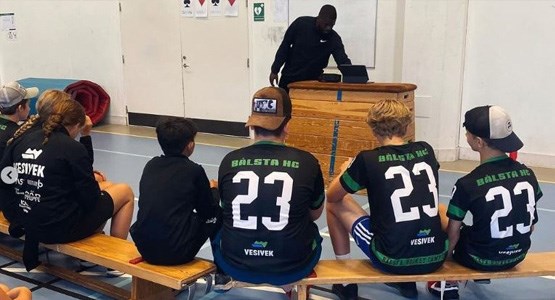 Killar sitter och lyssnar på en bänk i en gympasal