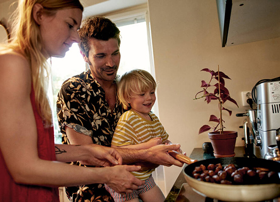 En mamma, pappa och ett barn står i köket och steker köttbullar.