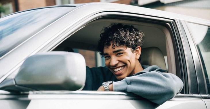 Ung, glad kille sitter i bil med nedrullad ruta.