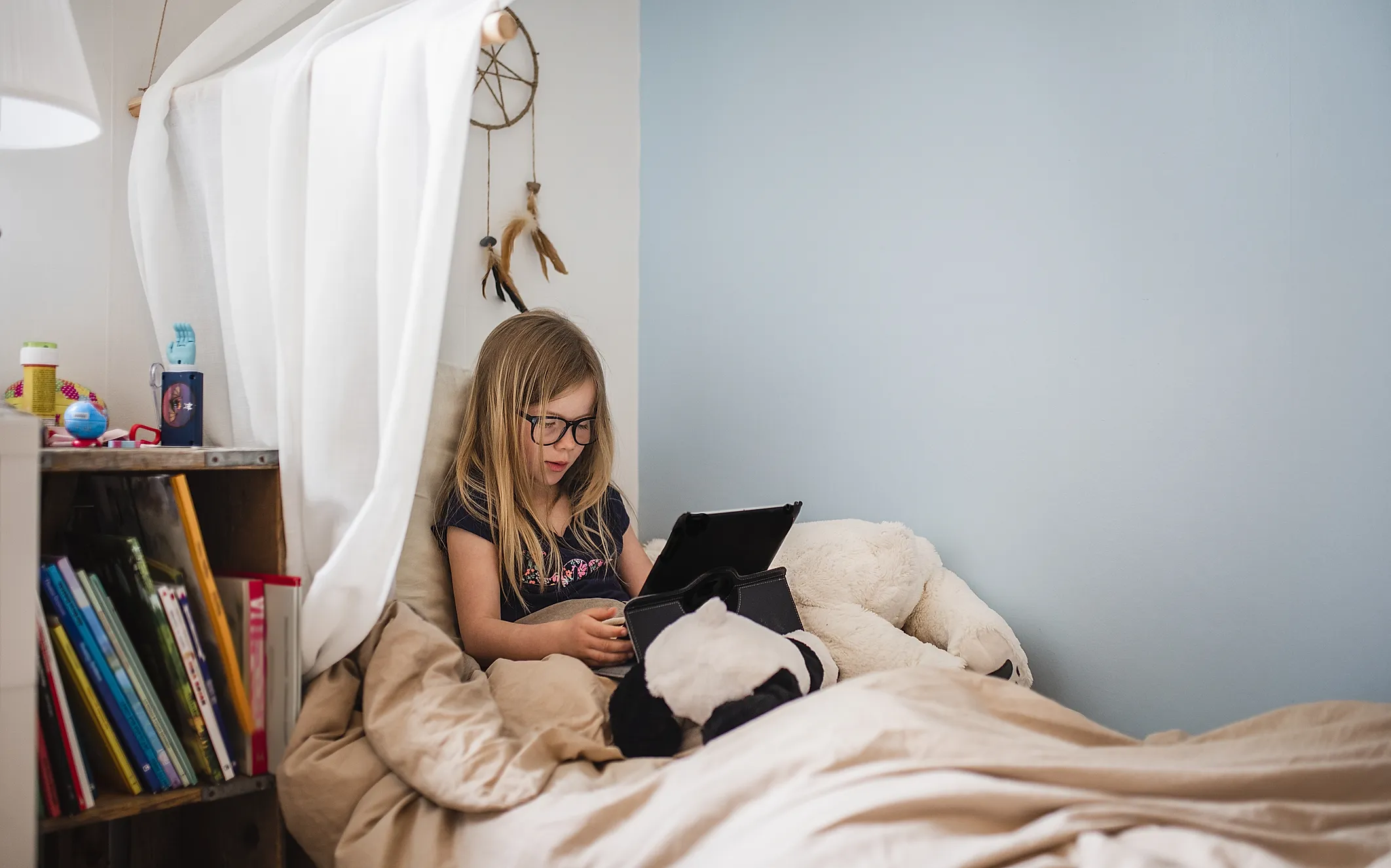 Flicka i tioårsåldern sitter i säng med ipad.