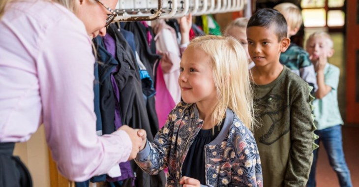 Ett barn i småskoleålder tar i hand med sin pedagog och ler.
