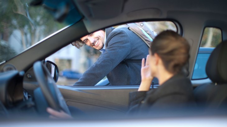 Kvinna kör iväg i bil medan hon vinkar till en man.