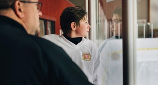 Pojke i hockeykläder tillsammans med ledare