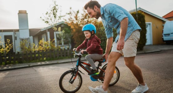 Ett barn övar på att cykla tillsammans med sin pappa.